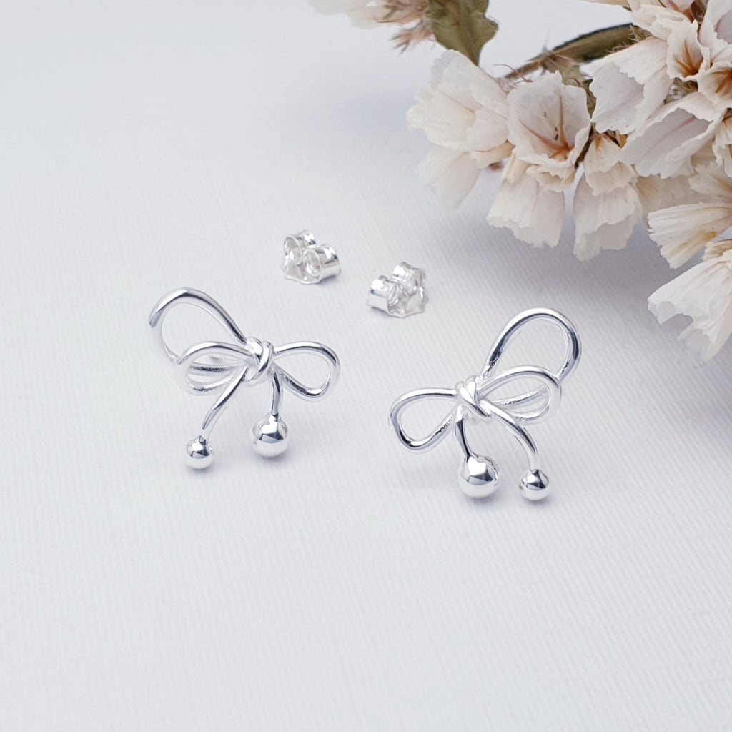 Silver bow-shaped earrings on a light surface with flowers in the background