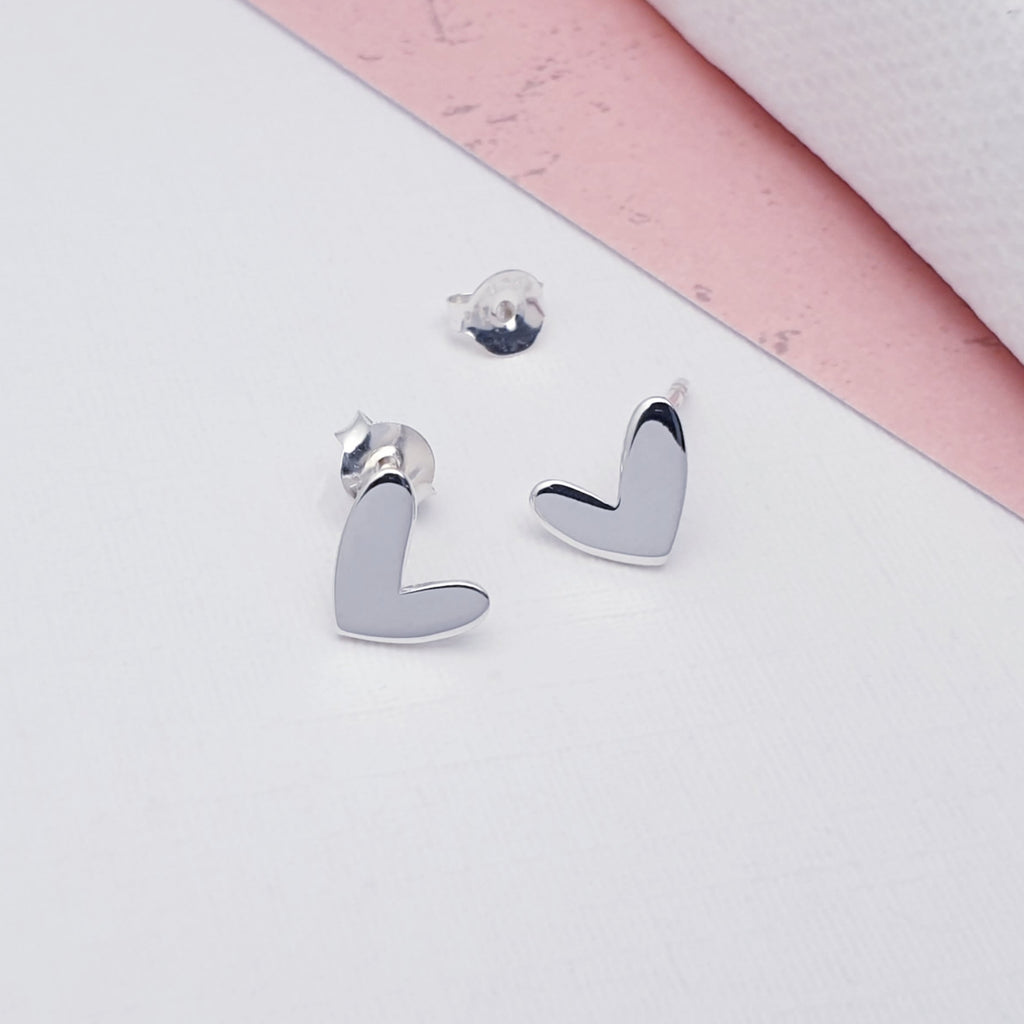 Heart-shaped silver earrings on a light pink and white background