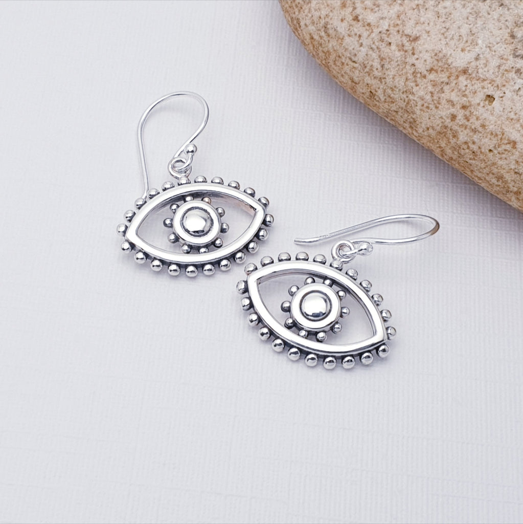 Silver eye-shaped earrings on a light gray background with a stone.