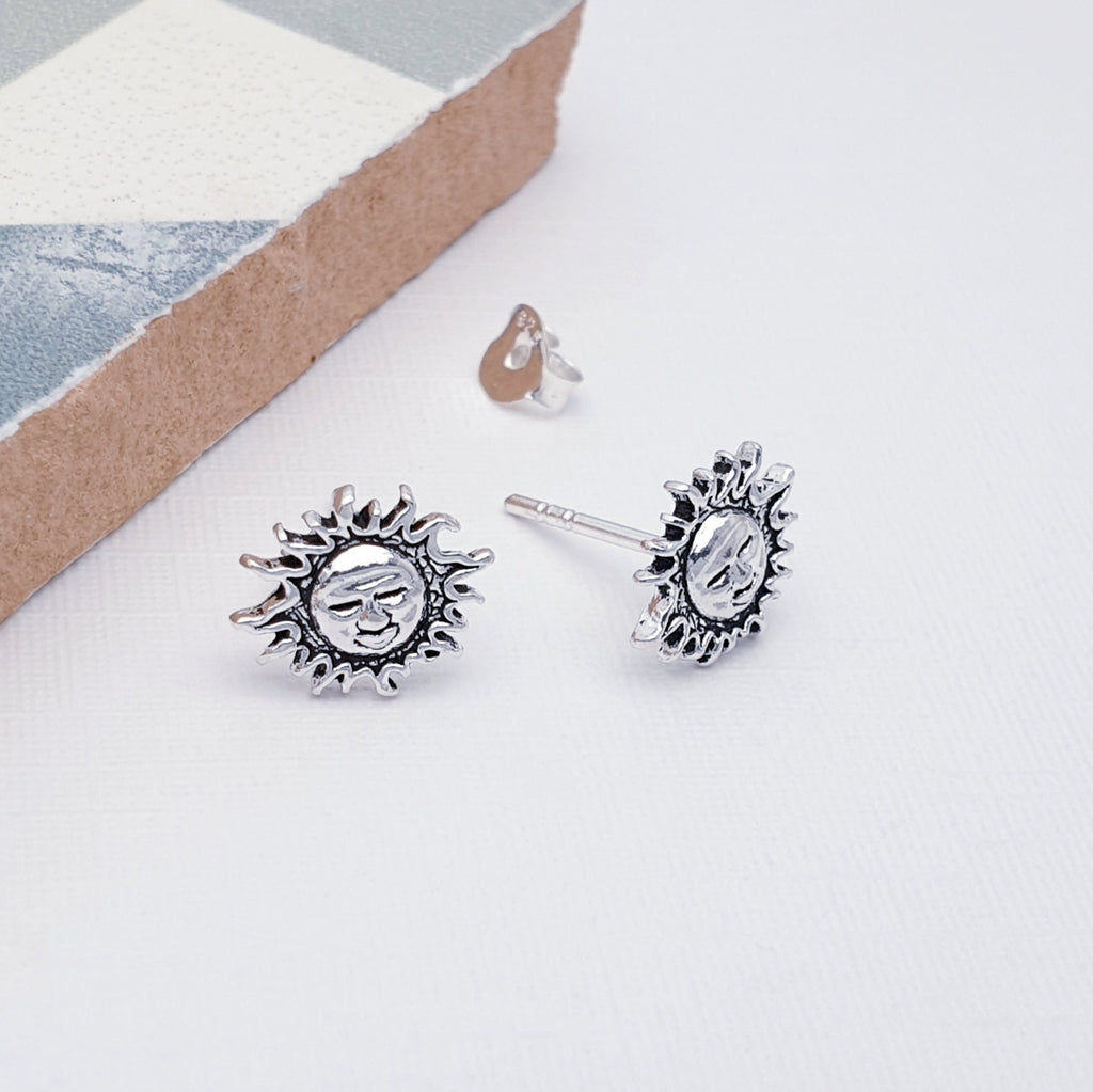 Silver sun-shaped earrings on a light gray surface with a neutral background