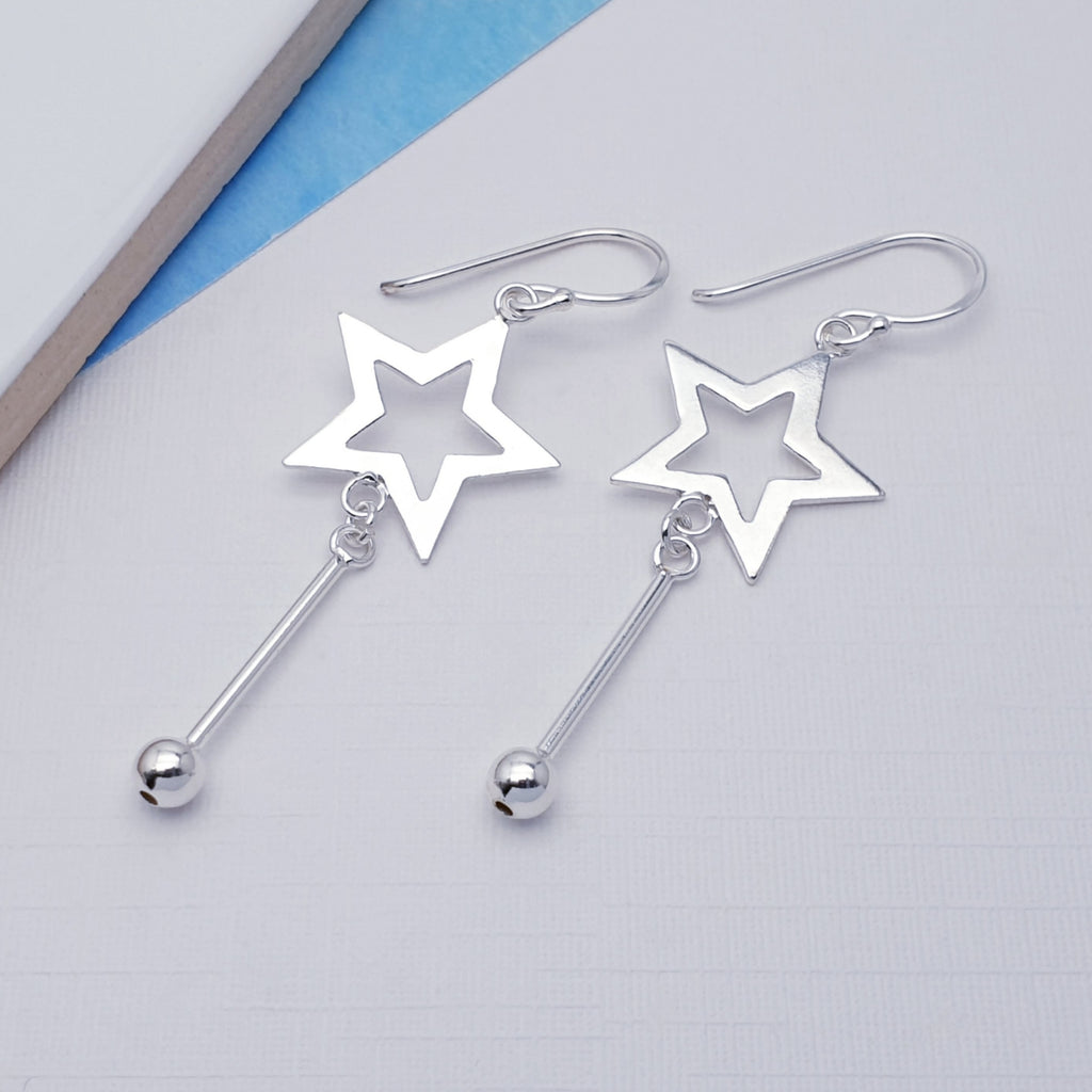Silver star-shaped earrings with dangling beads on a light gray background