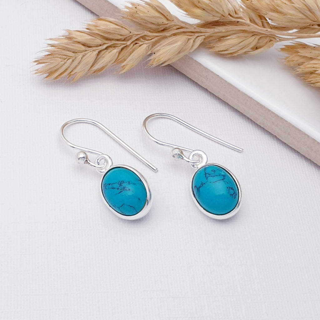 Our simple turquoise oval earrings displayed on a white background with a white tile and autumn foliage decorating the background