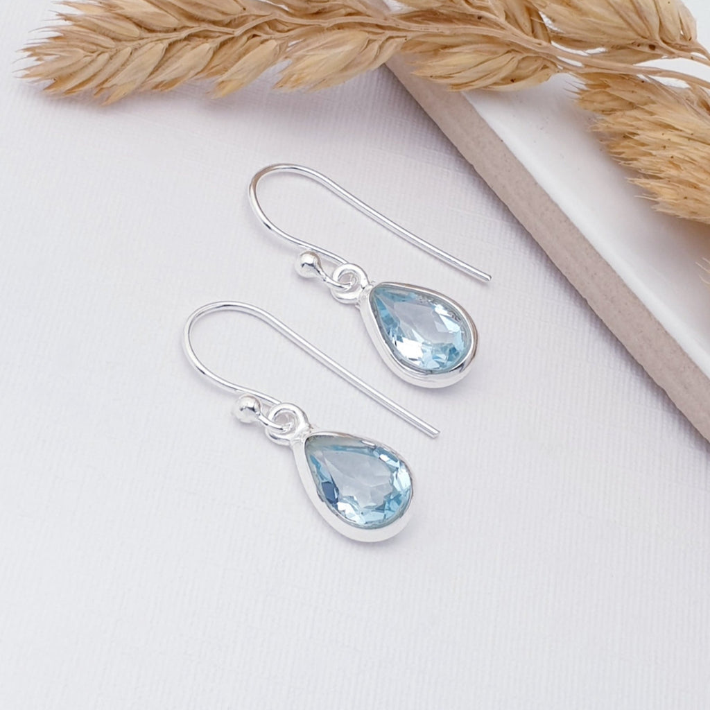 Blue topaz single teardrop earrings displayed on a white background with autumnal foliage as decoration