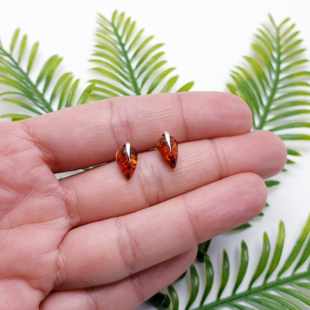 Dainty toffee amber leaf design stud earrings in a hand with green foliage behind