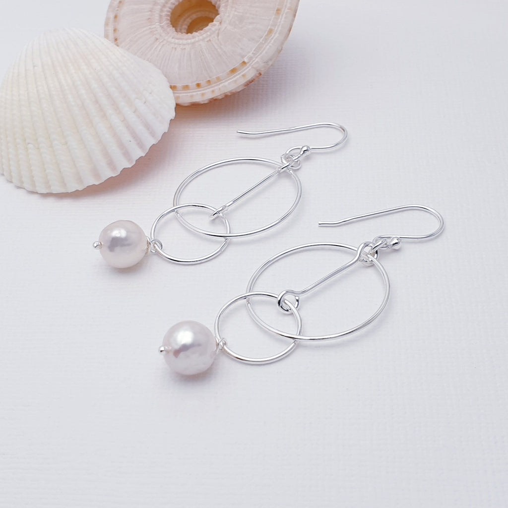 Our Pearl Funky Circles Earrings are perfect for everyday wear or special occasions.  Add an elegant, timeless touch to your ensemble with these Pearl Sterling Silver Funky Circles Earrings. Featuring two connected rings with a Pearl drop, these delicate pieces are sure to elevate any look with a classic, sophisticated style. 