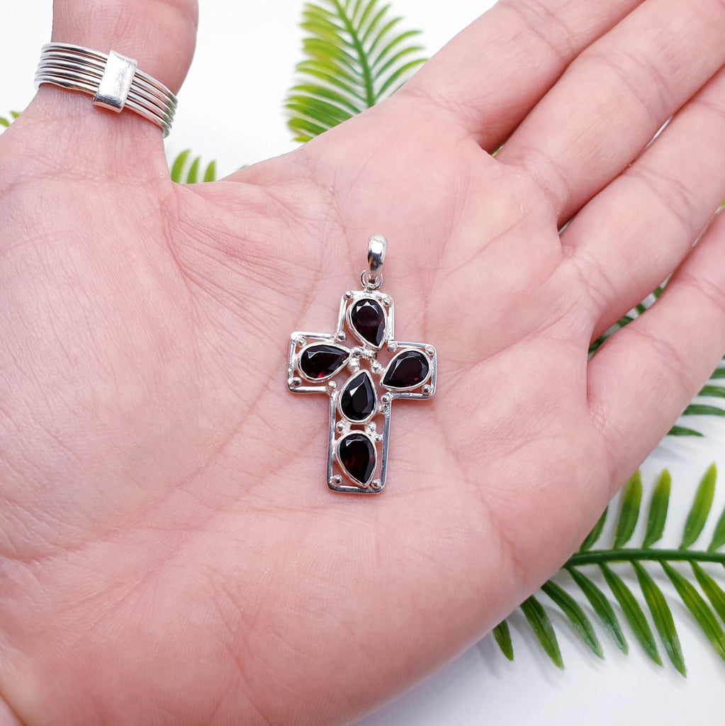 sterling silver cross pendant with garnet teardrop gemstones placed in the palm of a hand.