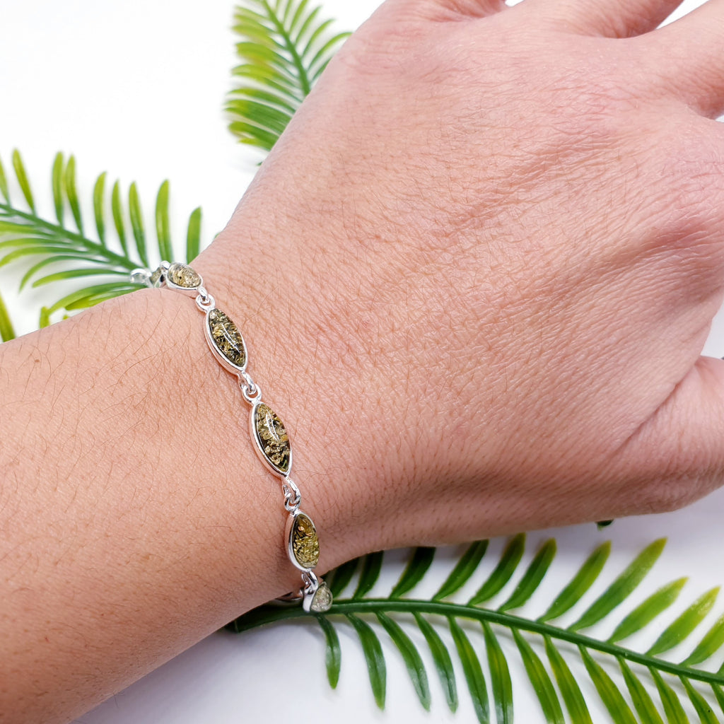 A Green Amber Sterling Silver Bracelet with marquise shaped stones on a wrist. Dainty and elegant with a classic look. green foliage behind.