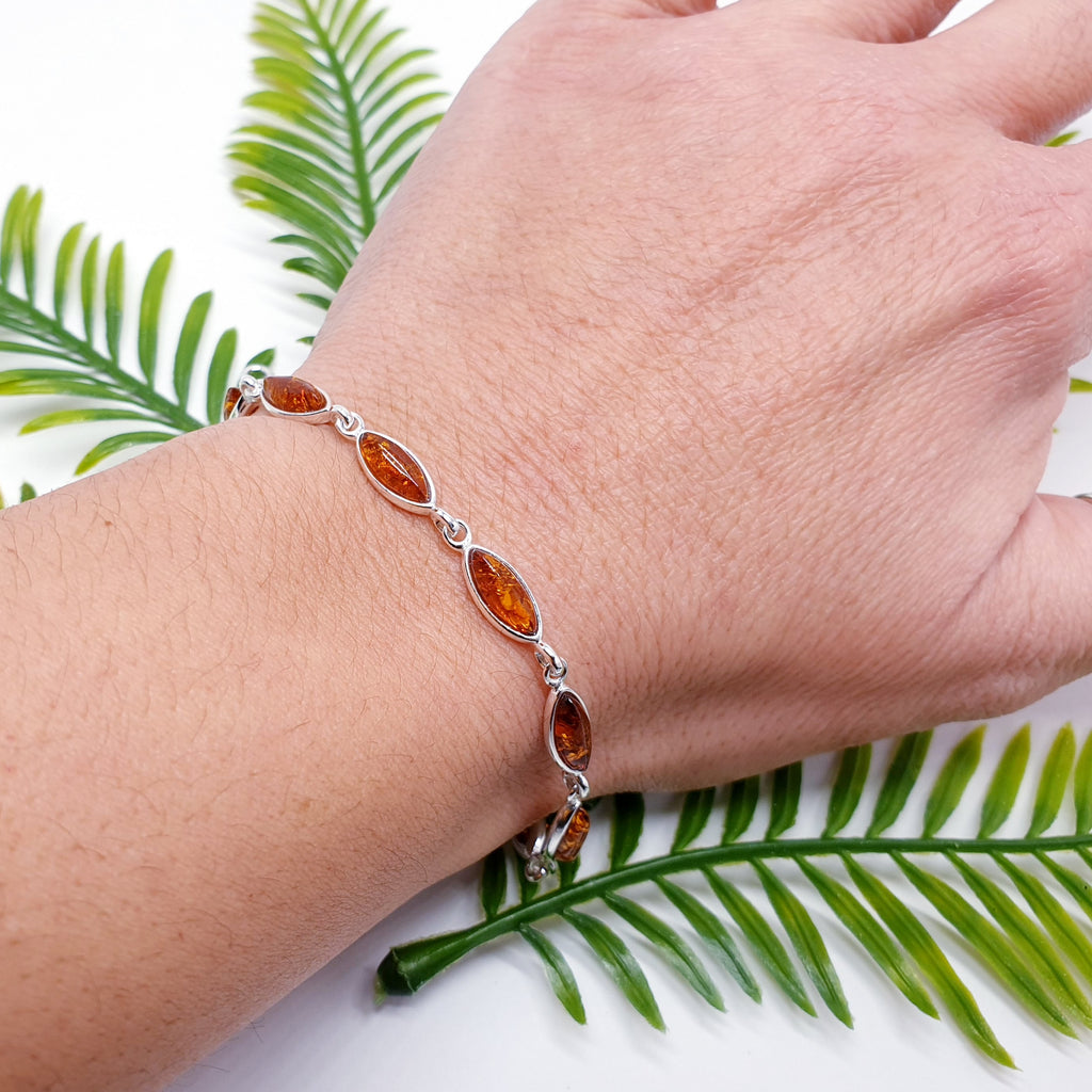 A Toffee Amber Sterling Silver Bracelet with marquise shaped stones on a wrist. Dainty and elegant with a classic look. green foliage behind.