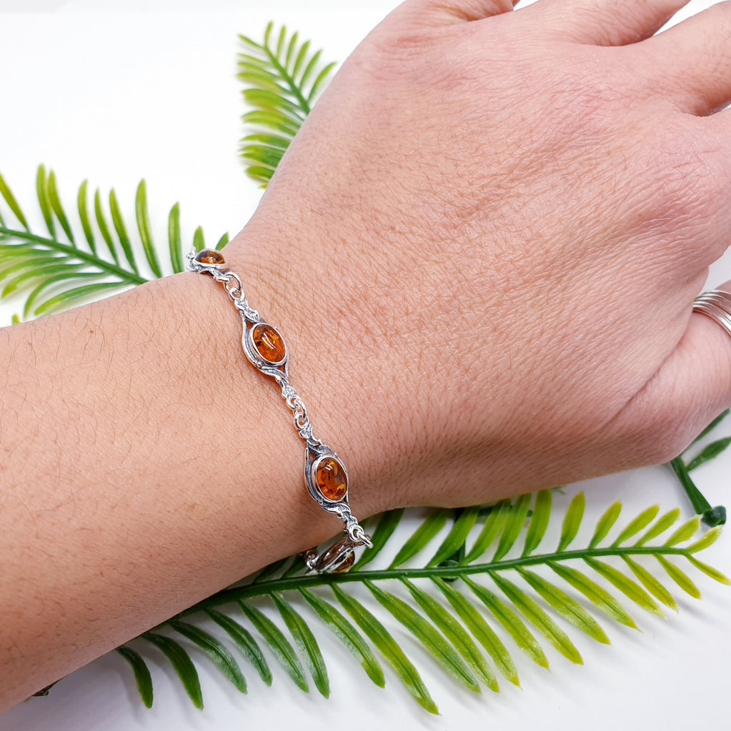 A toffee genuine amber vintage style bracelet, with sterling silver, on a wrist. With green foliage behind.
