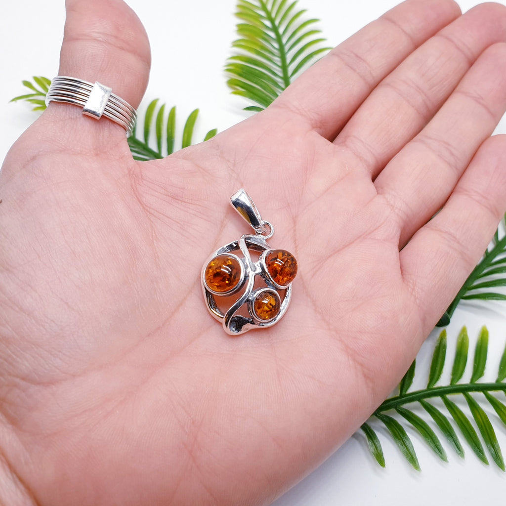 a toffee Amber Sterling Silver pendant in the palm of a hand