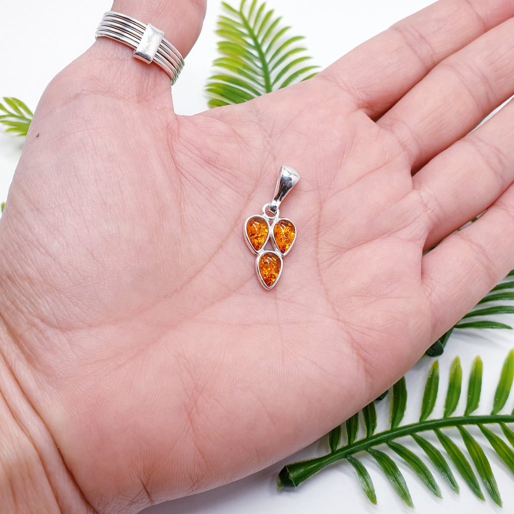 a toffee amber pendant with three teardrop shaped gemstones in a sterling silver setting, placed in the palm of a hand