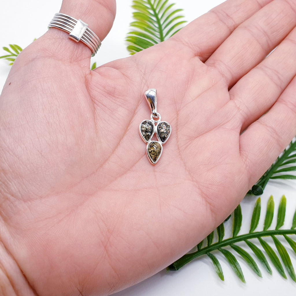 a green amber pendant with three teardrop shaped gemstones in a sterling silver setting, placed in the palm of a hand