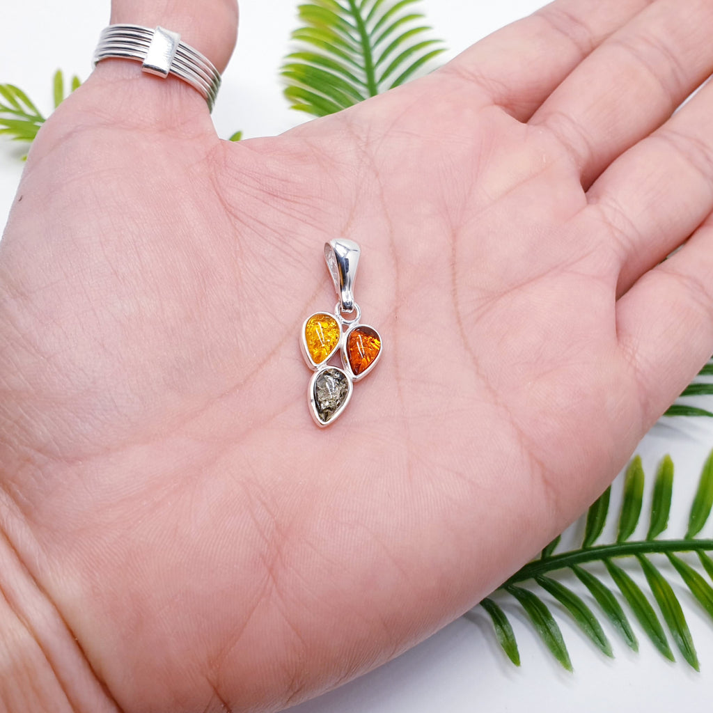 a mixed amber pendant with three teardrop shaped gemstones in a sterling silver setting, placed in the palm of a hand