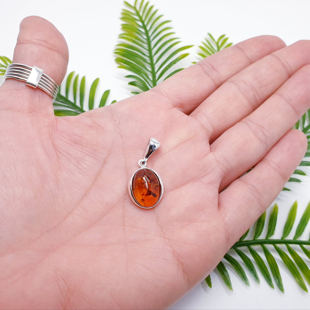 dainty oval vintage style amber pendant in the palm of a hand