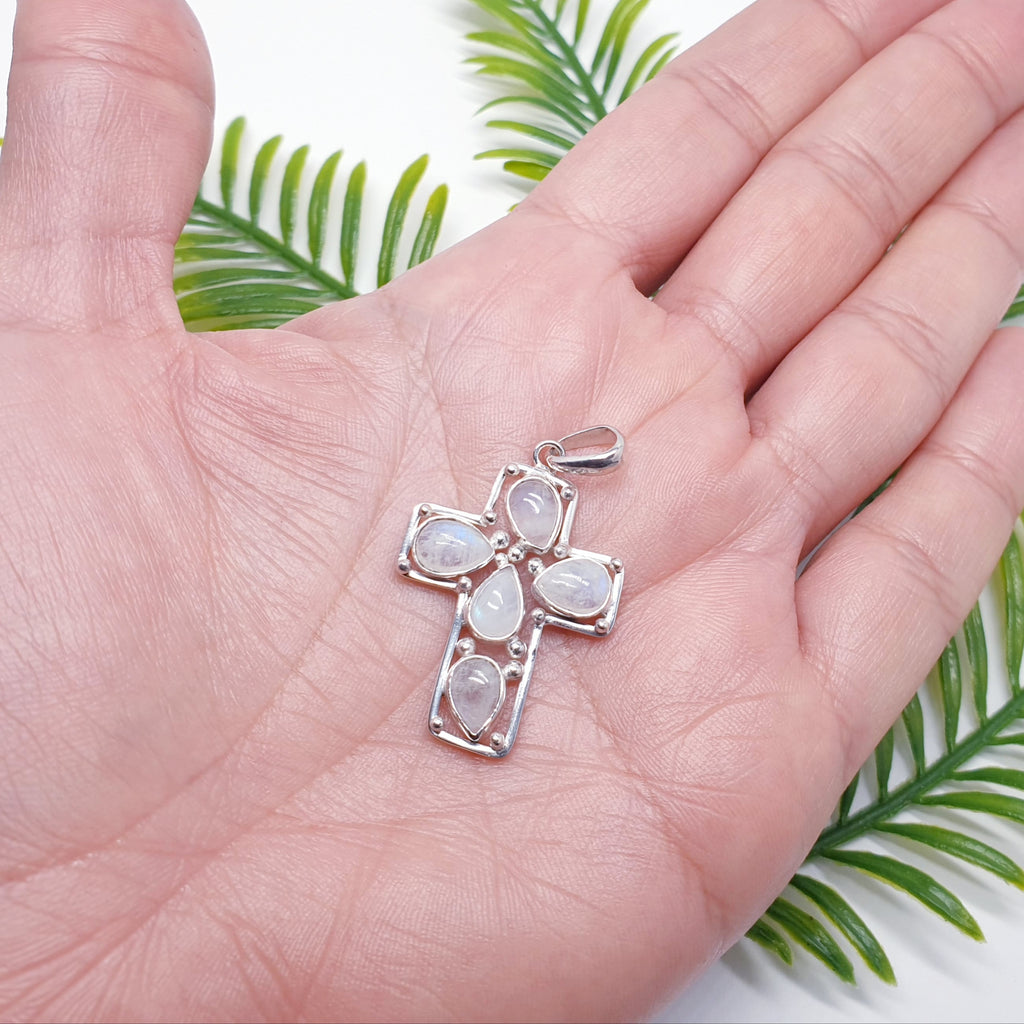 Sterling silver cross pendant with teardrop moonstone gemstones in the palm of a hand