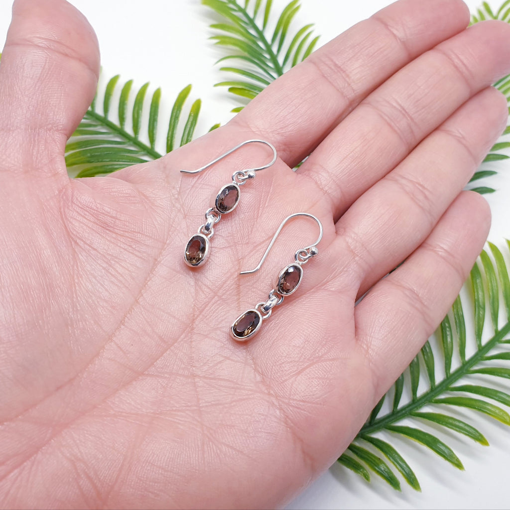 A pair of dainty smoky quartz and sterling silver earrings in the palm of a ahnd.