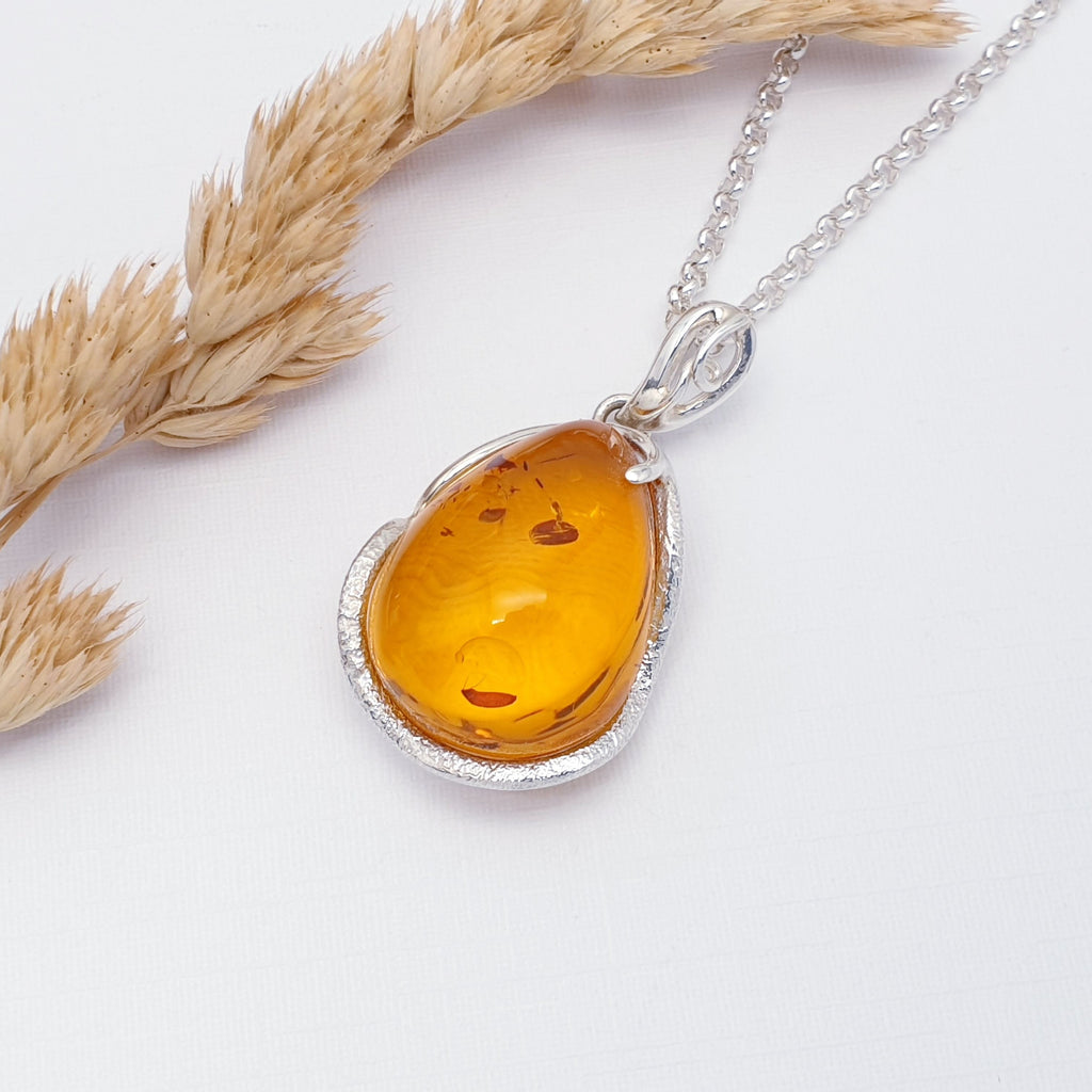 Our Toffee Amber Izabella pendant on a Medium Belcher chain, displayed flat on a white background with foliage decorations