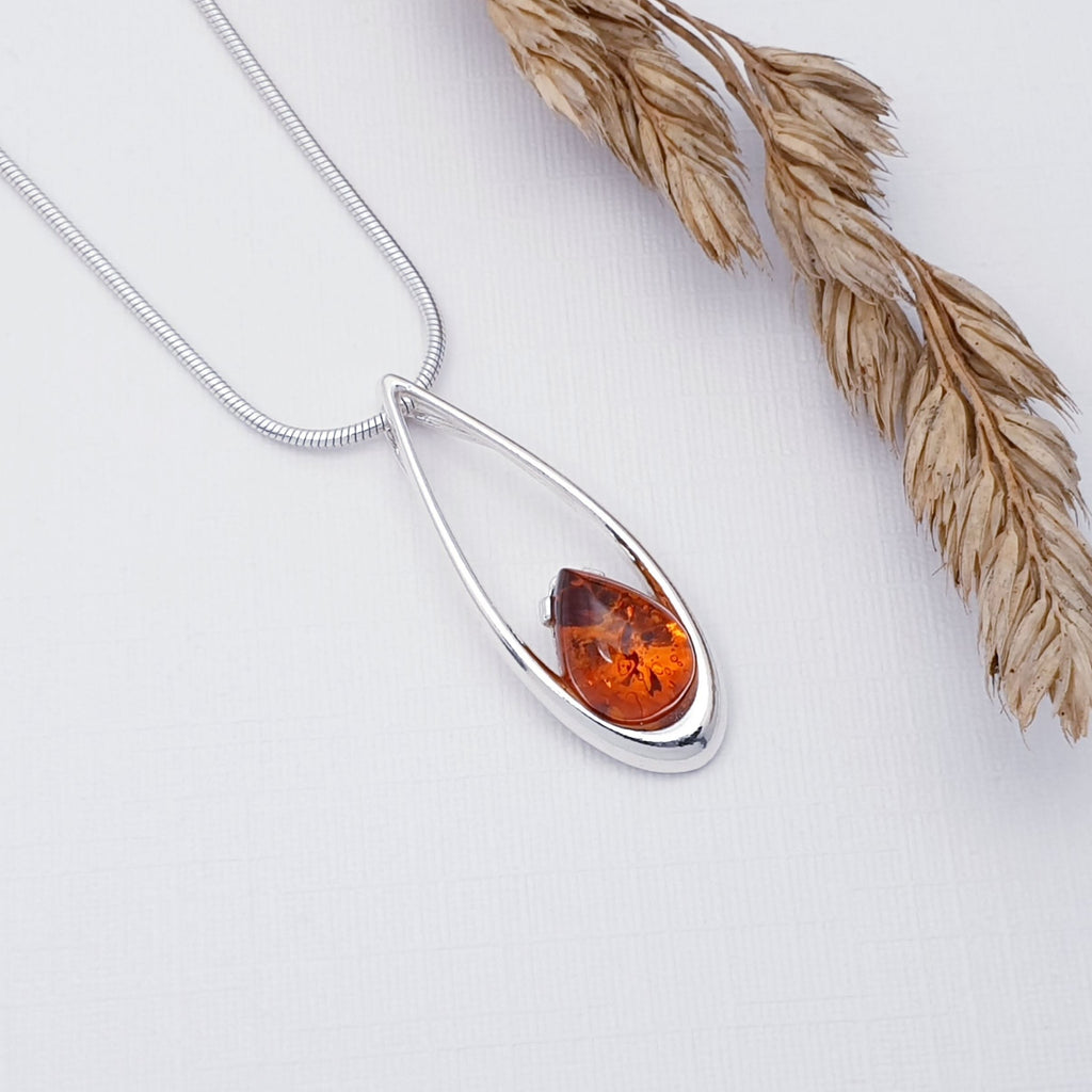 Our Amber pip pendant strung on a fine snake chain, displayed flat on a white background with autumn foliage decoration