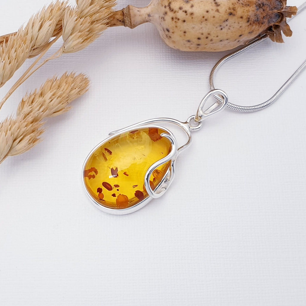 Our Toffee Amber Luiza pendant strung on a medium snake chain, displayed flat on a white background with autumn foliage decorations