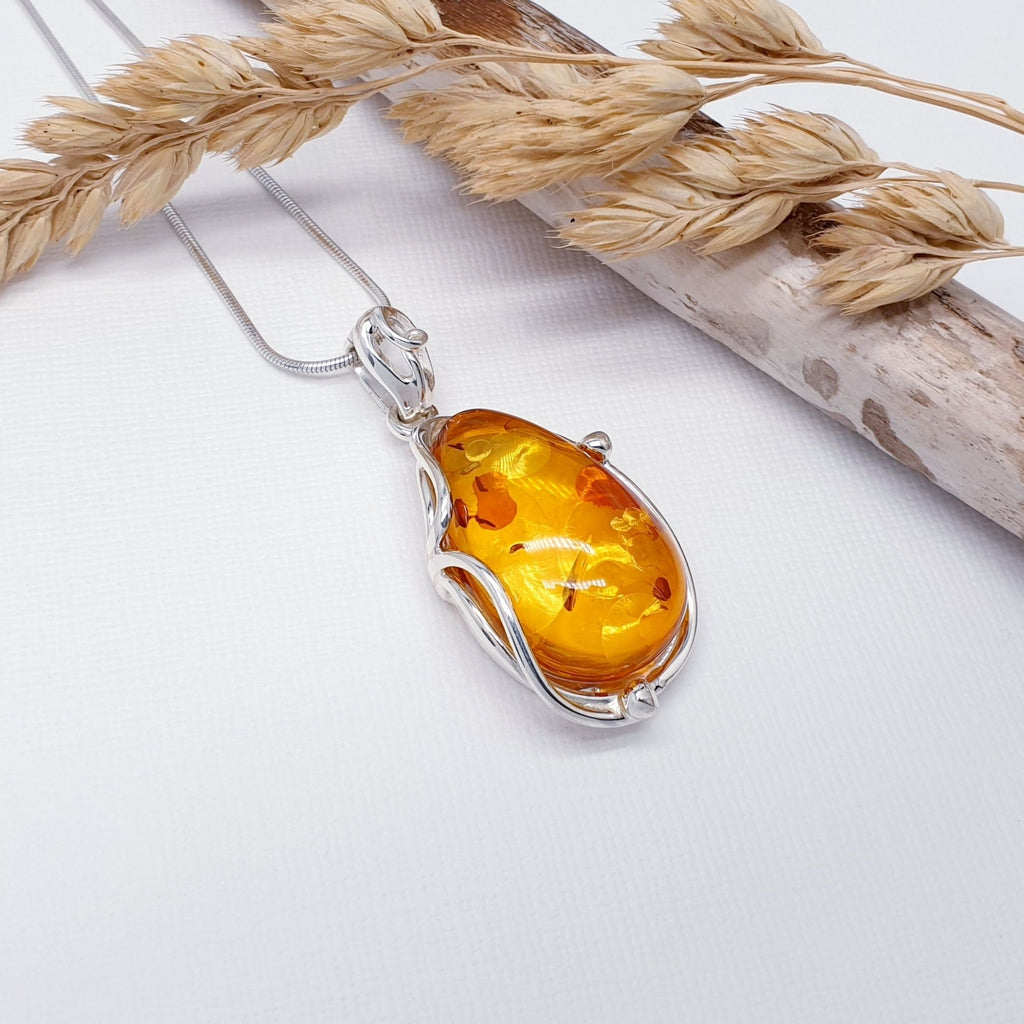 Our Toffee Amber Tosia pendant strung on a medium snake chain, layed flat on a white background with driftwood and autumn foliage decorations