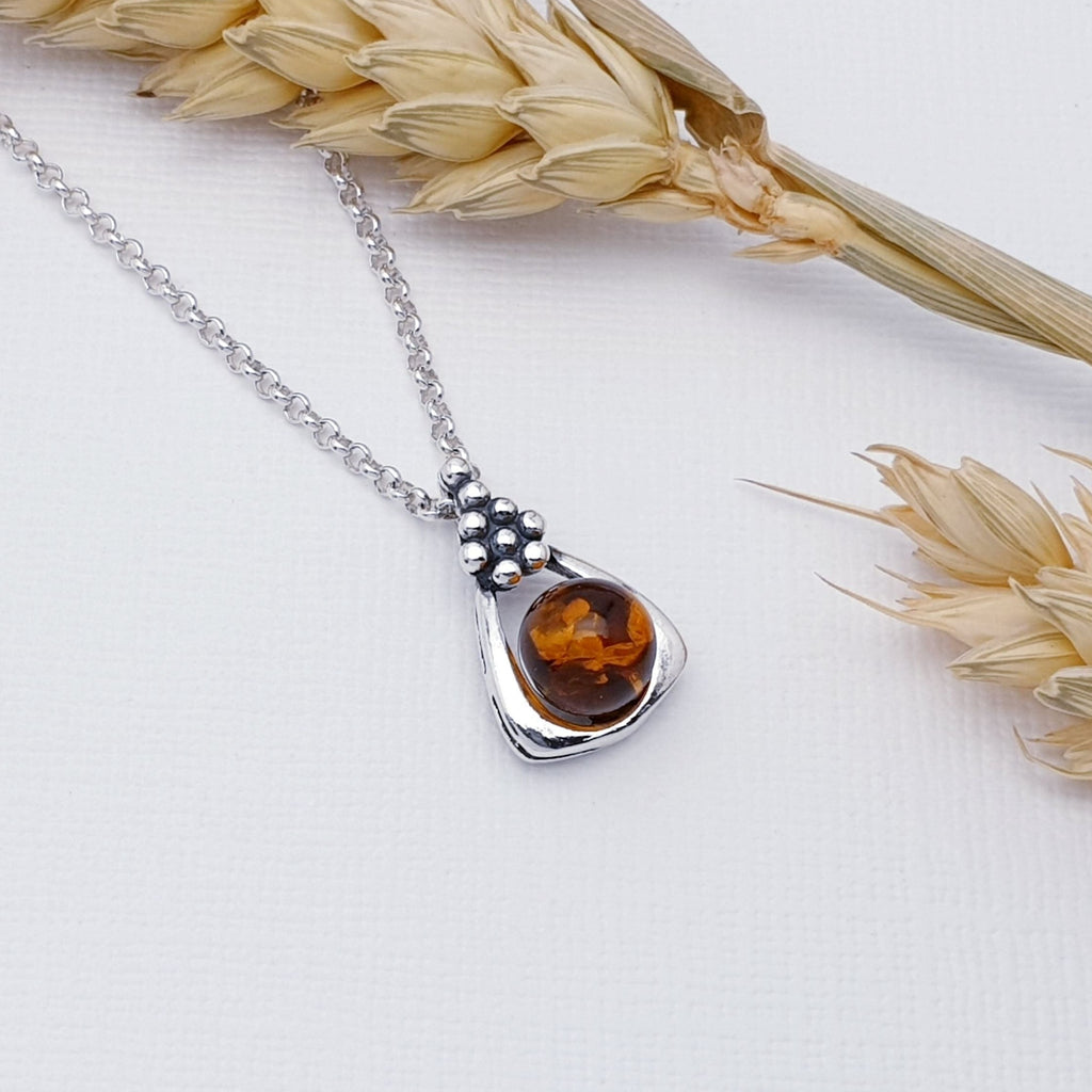 Our toffee amber grapevine pendant strung on a fine belcher chain, against a white background with autumn foliage decorations