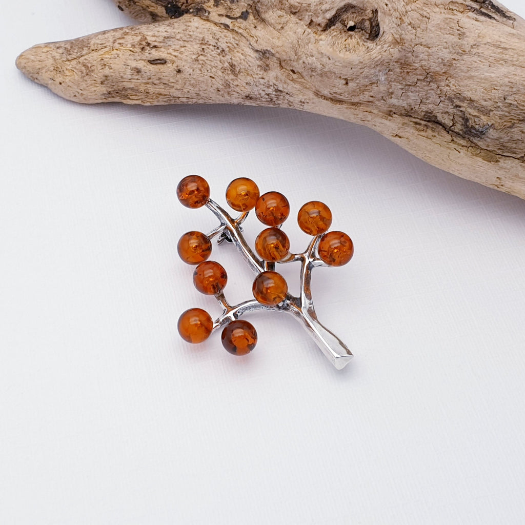 Our Toffee Amber tree brooch displayed flat on a white background with driftwood as decoration