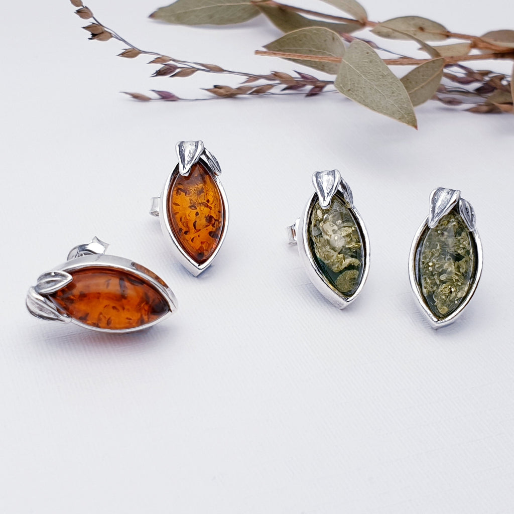 Two pairs of our Amber botanical studs, one in toffee amber and the other in Green Amber. Displayed on a white background with foliage as decoration