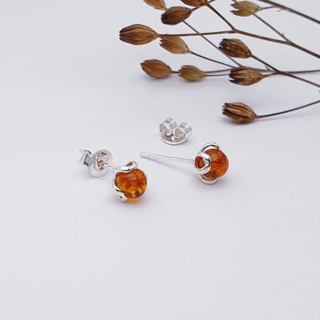 Our toffee amber flower bud studs displayed on a white background with autumn foliage as decoration