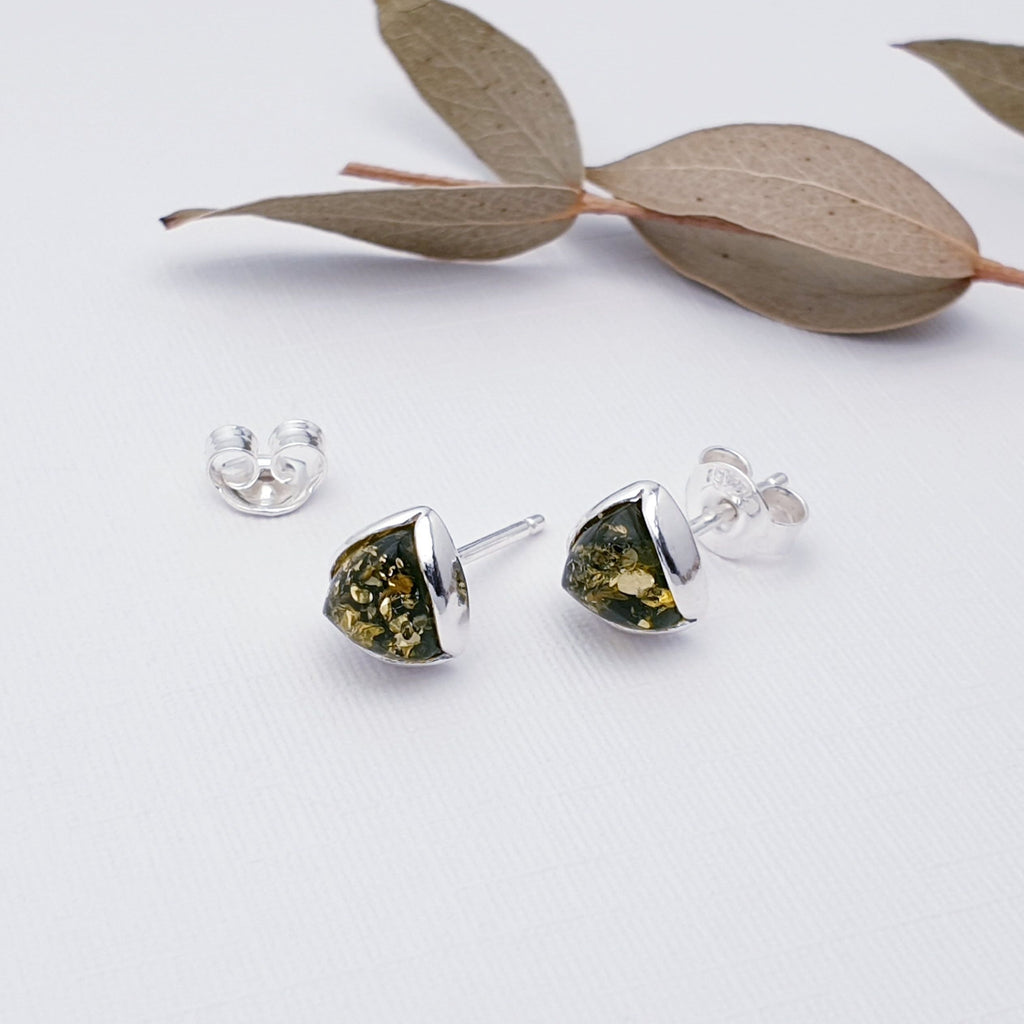 Our Green Amber Simple Triangle studs layed flat on a white background with leaf decorations