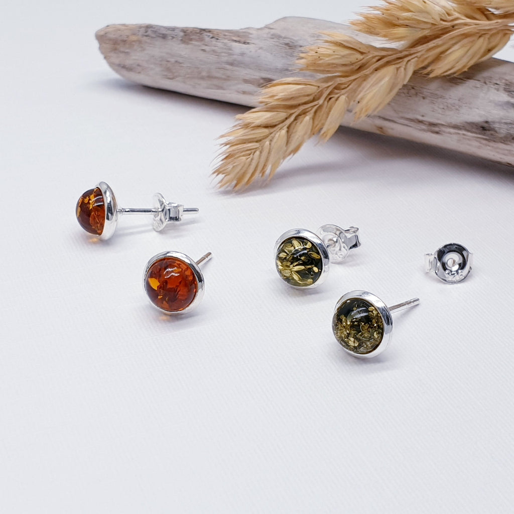 Two pairs of our Amber small round studs, one in green amber and the other in toffee amber. these are layed flat on a white background with wood and autumn foliage decorations