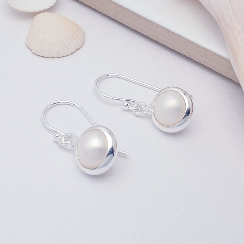 simple dainty pearl and sterling silver hook earrings, displayed on a white background with sea shells as decorations
