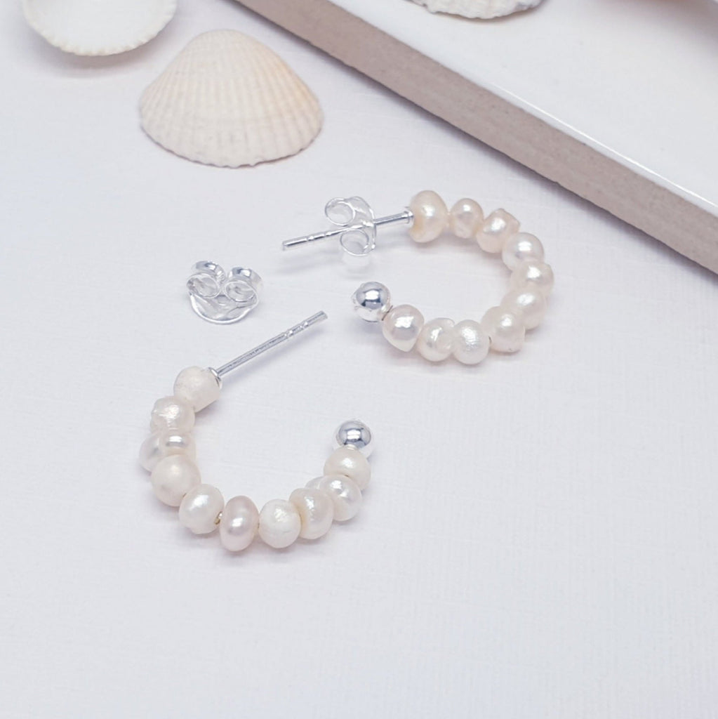 Beaded pearl half hoop sterling silver earrings, displayed on a white background with sea shells as decorations