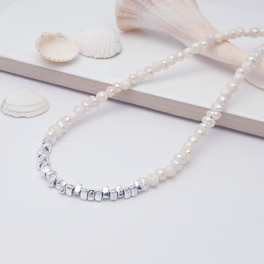 Pearl and sterling silver beaded, adjustable necklace, displayed on a white background with a white tile and sea shells as decorations