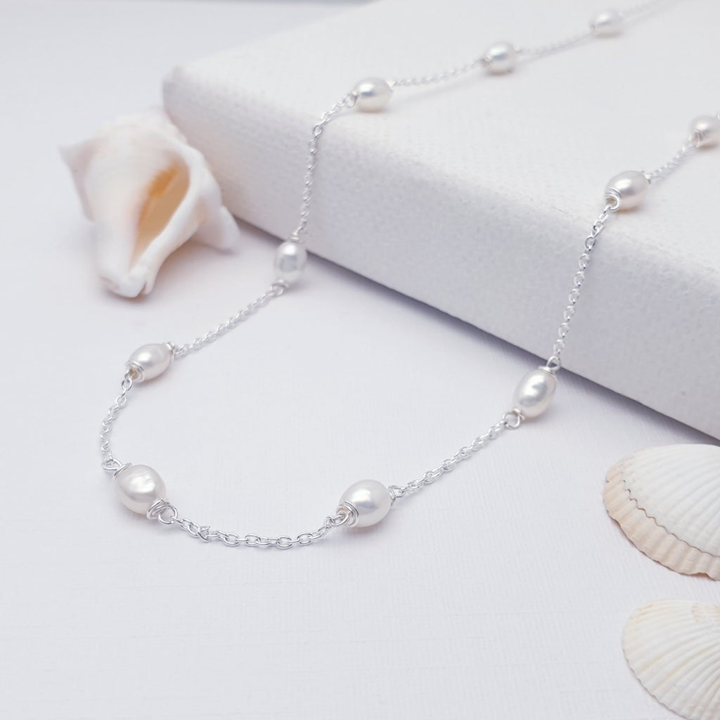 beaded pearl and sterling silver necklace displayed on a white background with sea shells as decorations
