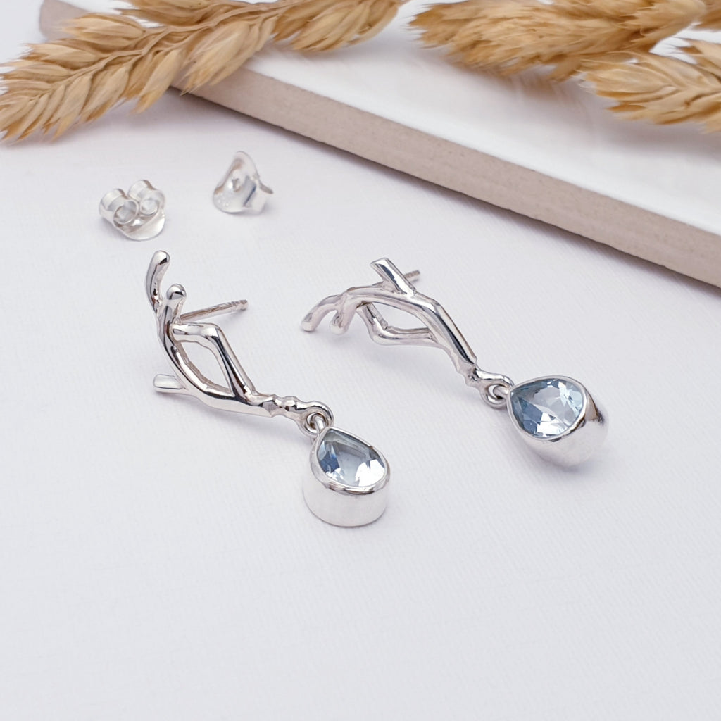 Our Blue topaz vine stud earrings displayed on a white background, with a tile and foliage as decortaions