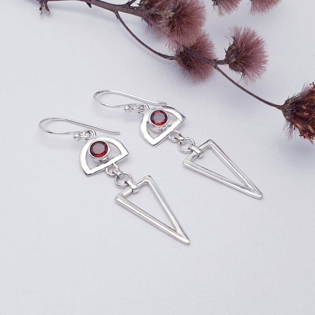 Sterling silver garnet hastate earrings on a white background with red foliage