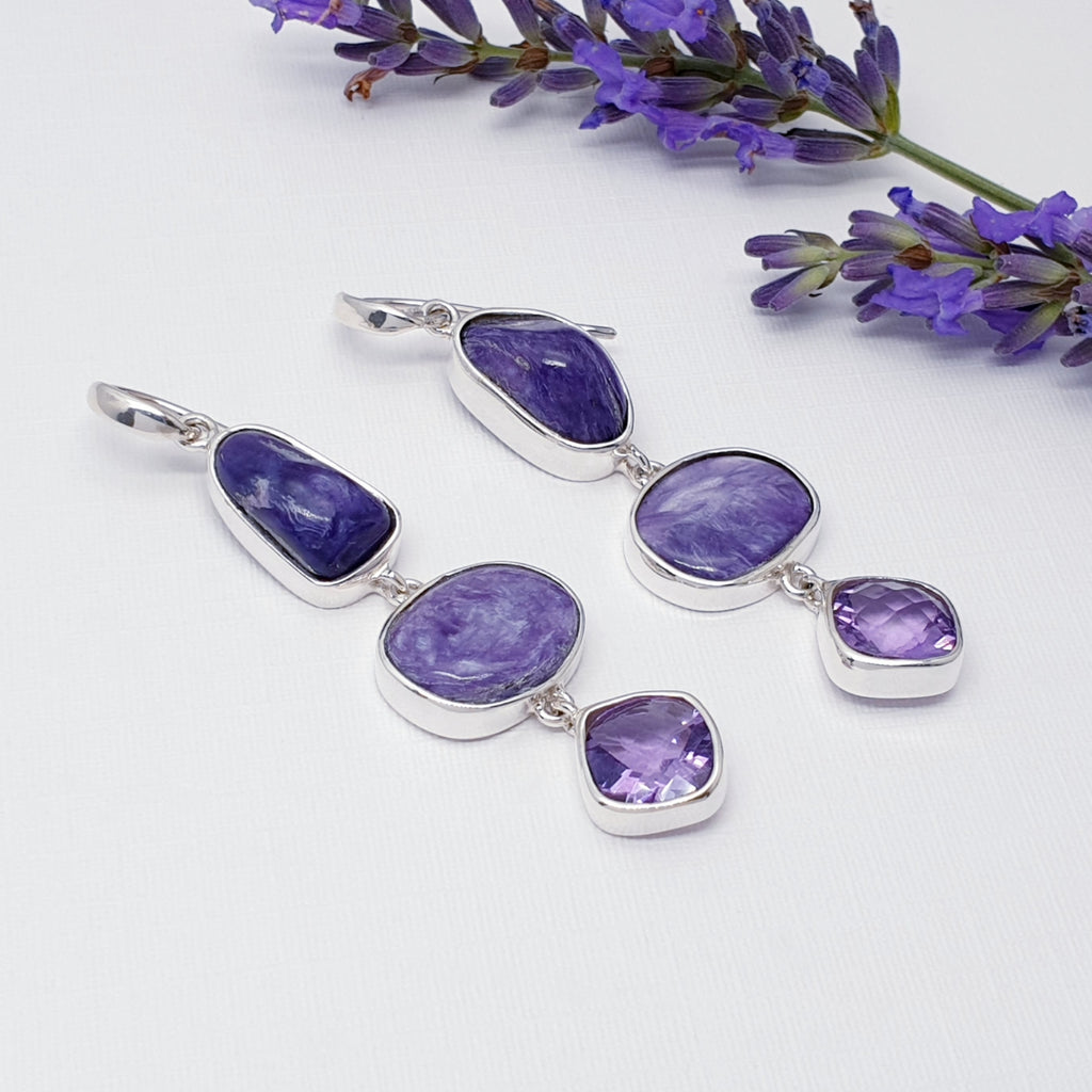 Charoite and Amethyst free form earrings on a white background with purple foliage 