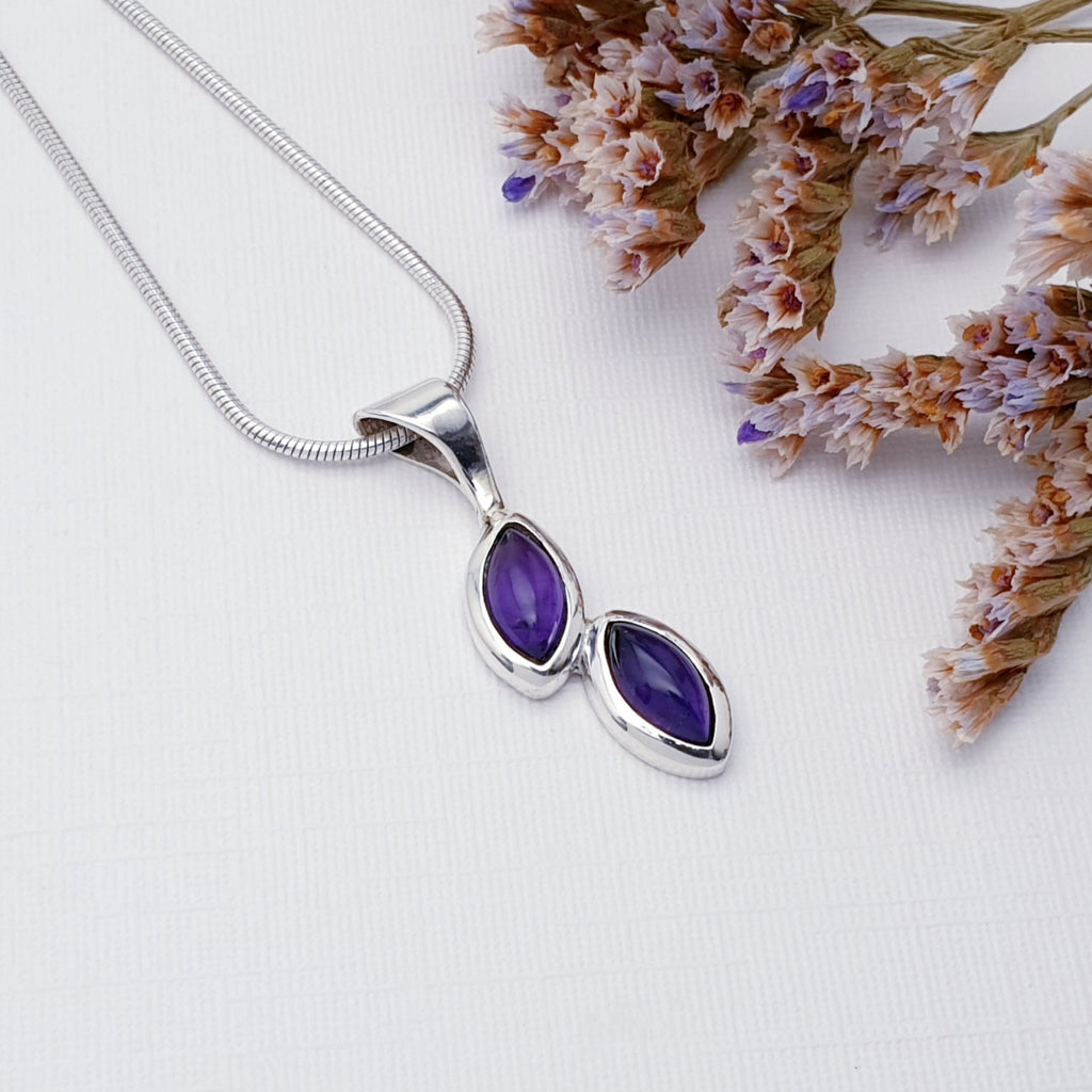 Amethyst falling petals pendant on a white background with purple and pink foliage in the top right corner.