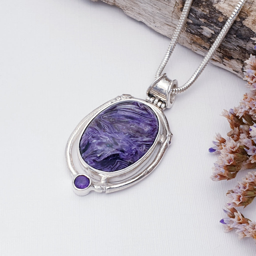 Charoite and amethyst pendant, Charoite being the made stone. On a white background with bar, pink and purple foliage