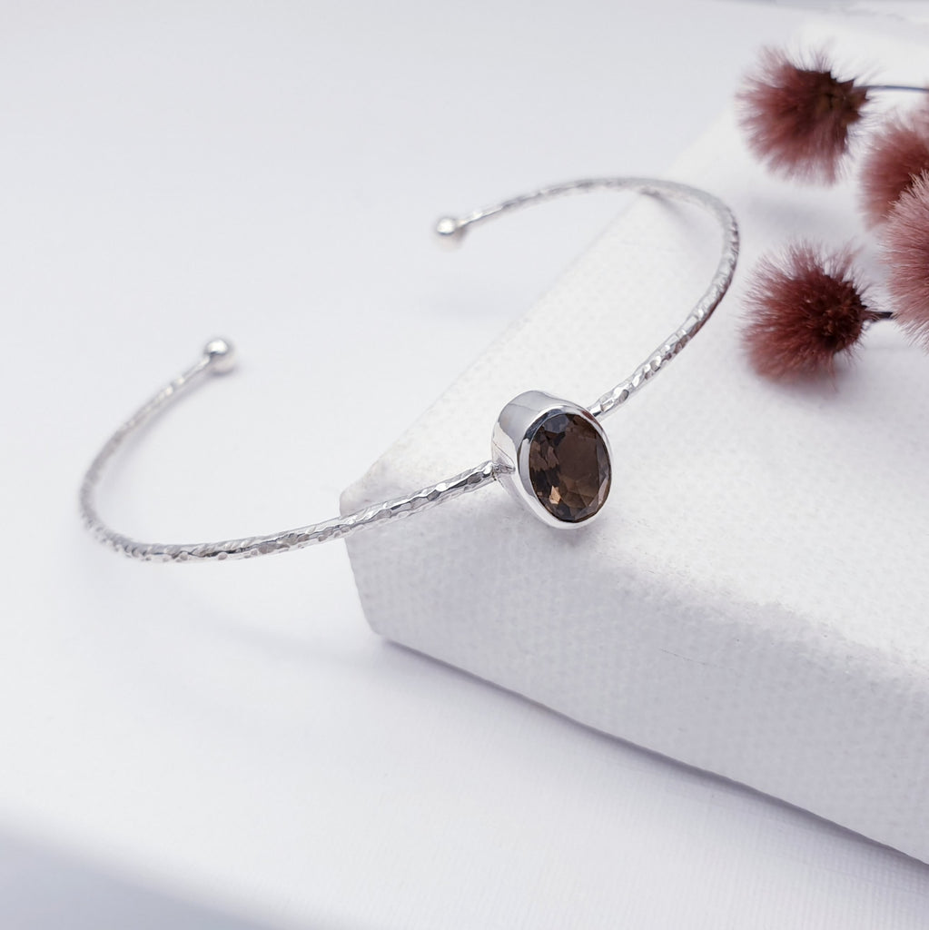 Our Smoky Quartz little stone cuff displayed on a white background with maroon coloured flowers as decoration