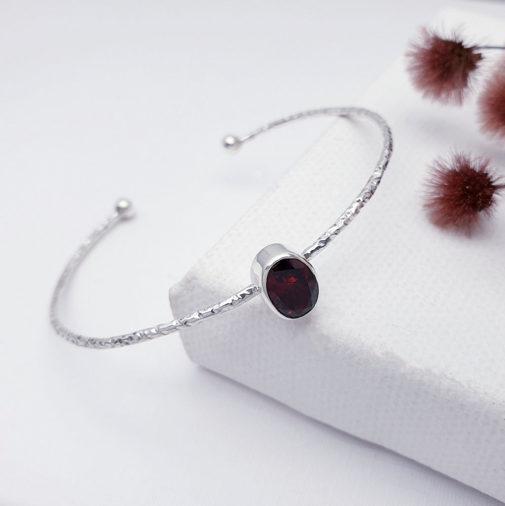 Our Garnet little stone cuff displayed on a white background with maroon flowers as decoration