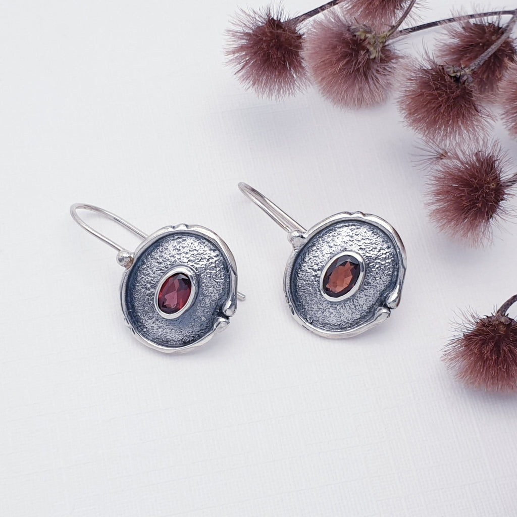 Garnet Oya Earrings on a white background with burgundy flowers in the top right corner