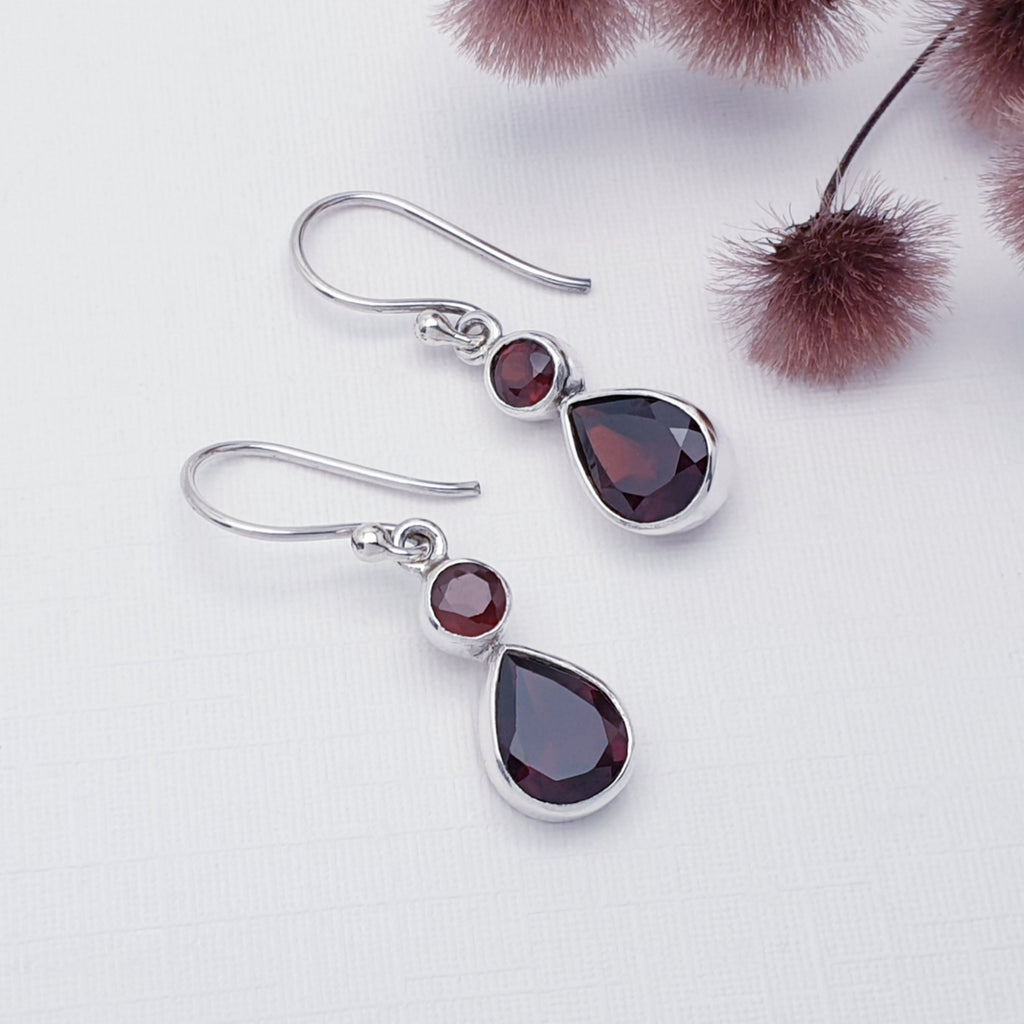 Garnet Aura Earrings on a white background with burgundy flowers in the top right corner