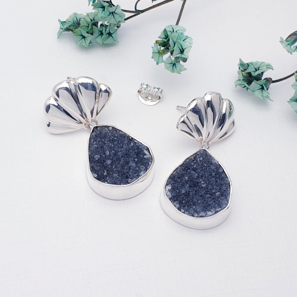 Our Druzy Quartz Scallop Earrings on a white background with small green flowers in the top half of the image. 