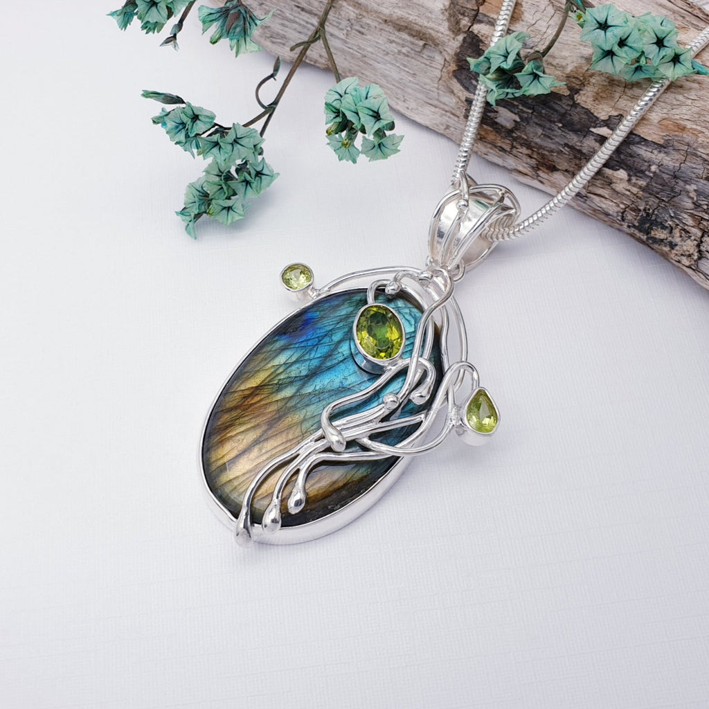 Labradorite and Peridot Sterling Silver Kusamba Pendant on a white background with bark and green filigree in the top right hand corner