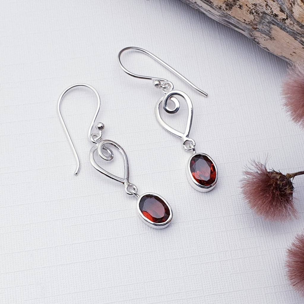 Our Garnet Love earrings displayed on a white background with maroon flowers and drift wood as decorations