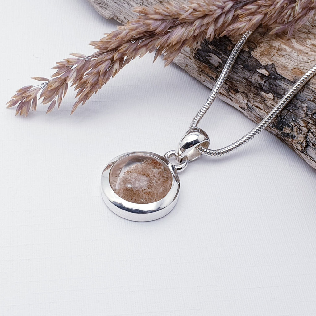 Our one-off lodolite round pendant strung on a heavy snake chain, displayed on a white background with wood and barley as decorations