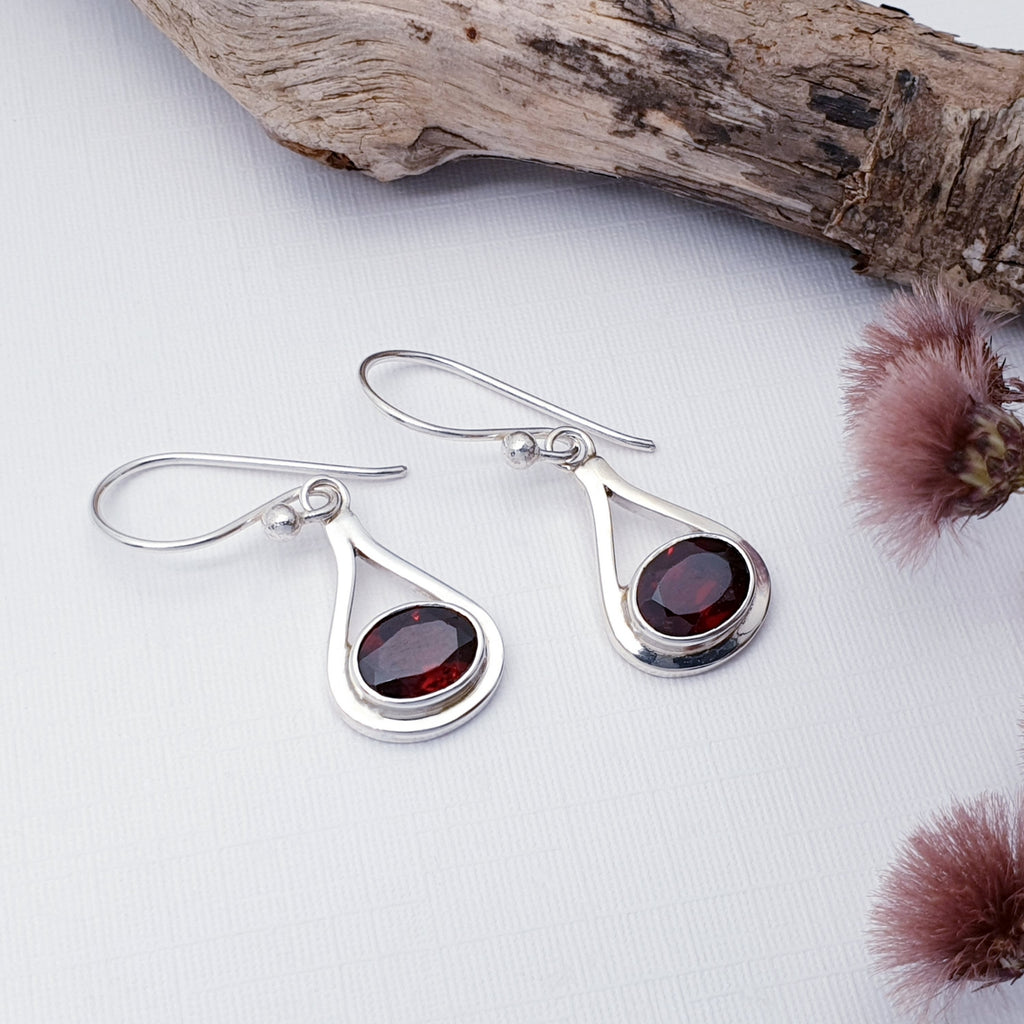 Our Garnet Valentina earrings displayed on a white background with wood and red flowers as decorations