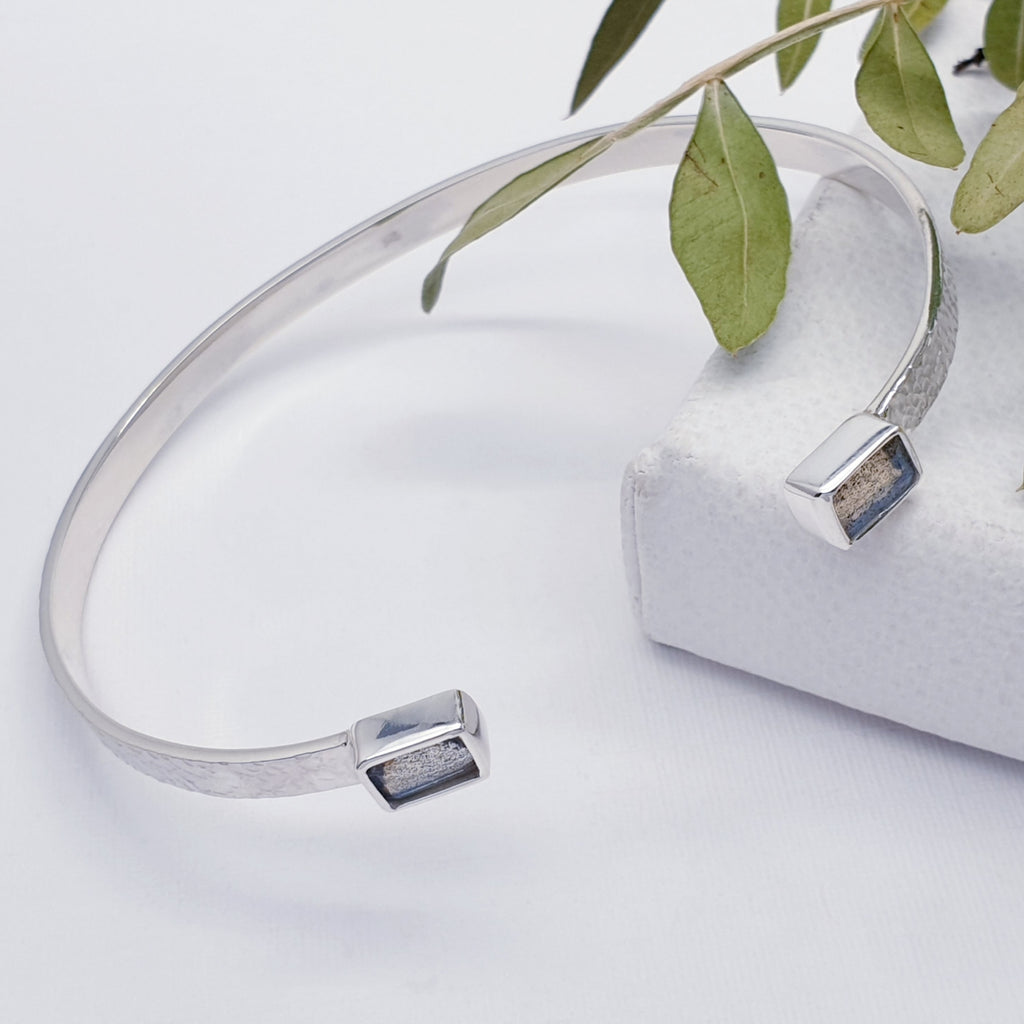 Our labradorite sterling silver hammered open cuff bracelet displayed on a white background with a leafy branch as decoration