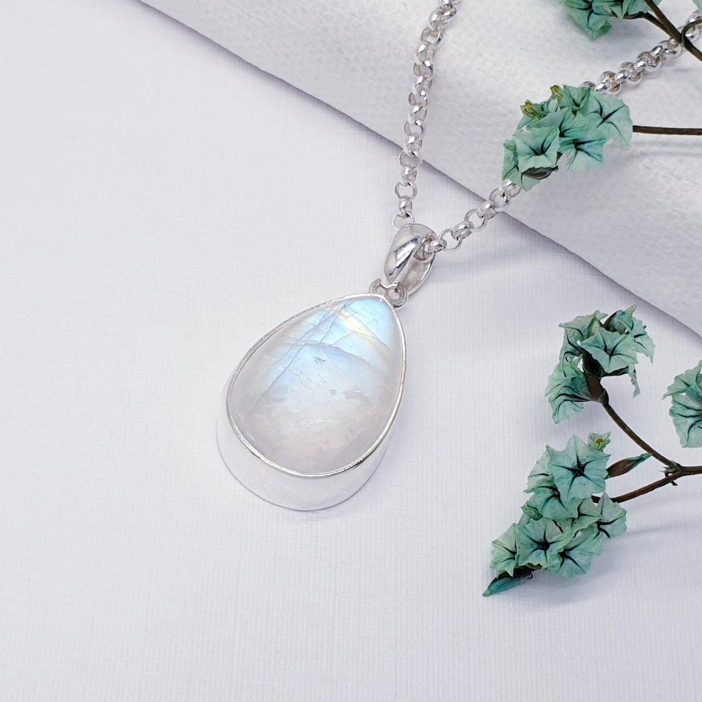 Our moonstone sterling silver teardrop pendant on a belcher link chain displayed on a white background with green flowers as decoration